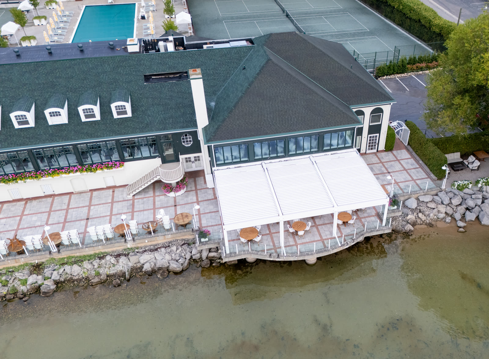 Wide commercial R-BLADE installation with screens, LED lighting, and lakeside seating &mdash; the magazine-grade amenity deck aesthetic multifamily marketing teams put on renderings and listing photos.