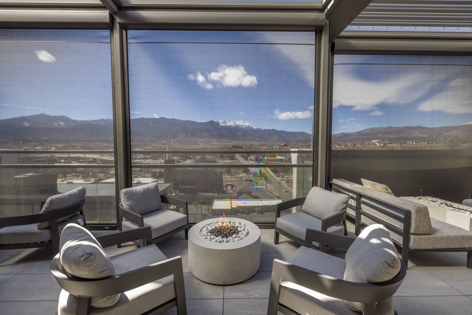 Louvered Azenco pergola enclosed with glass panels around a rooftop fire-table lounge. Manufacturer-network installation photo, not a CCSI project.