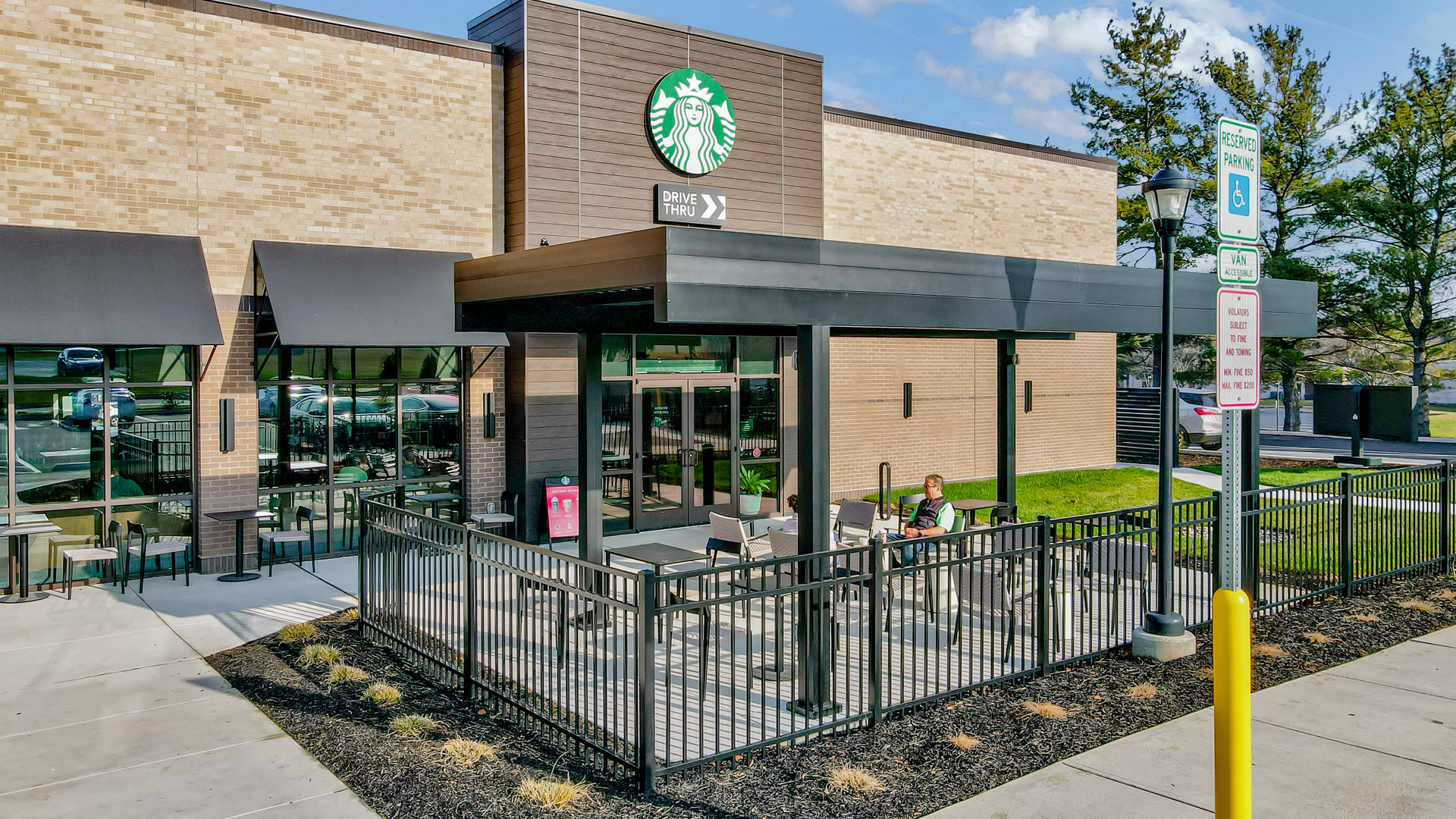 Full-black Azenco R-BLADE pergola in a modern commercial courtyard setting — the assembly Austin mixed-use developers and food-hall operators specify to anchor a ground-floor gathering zone against a mid-rise building envelope.