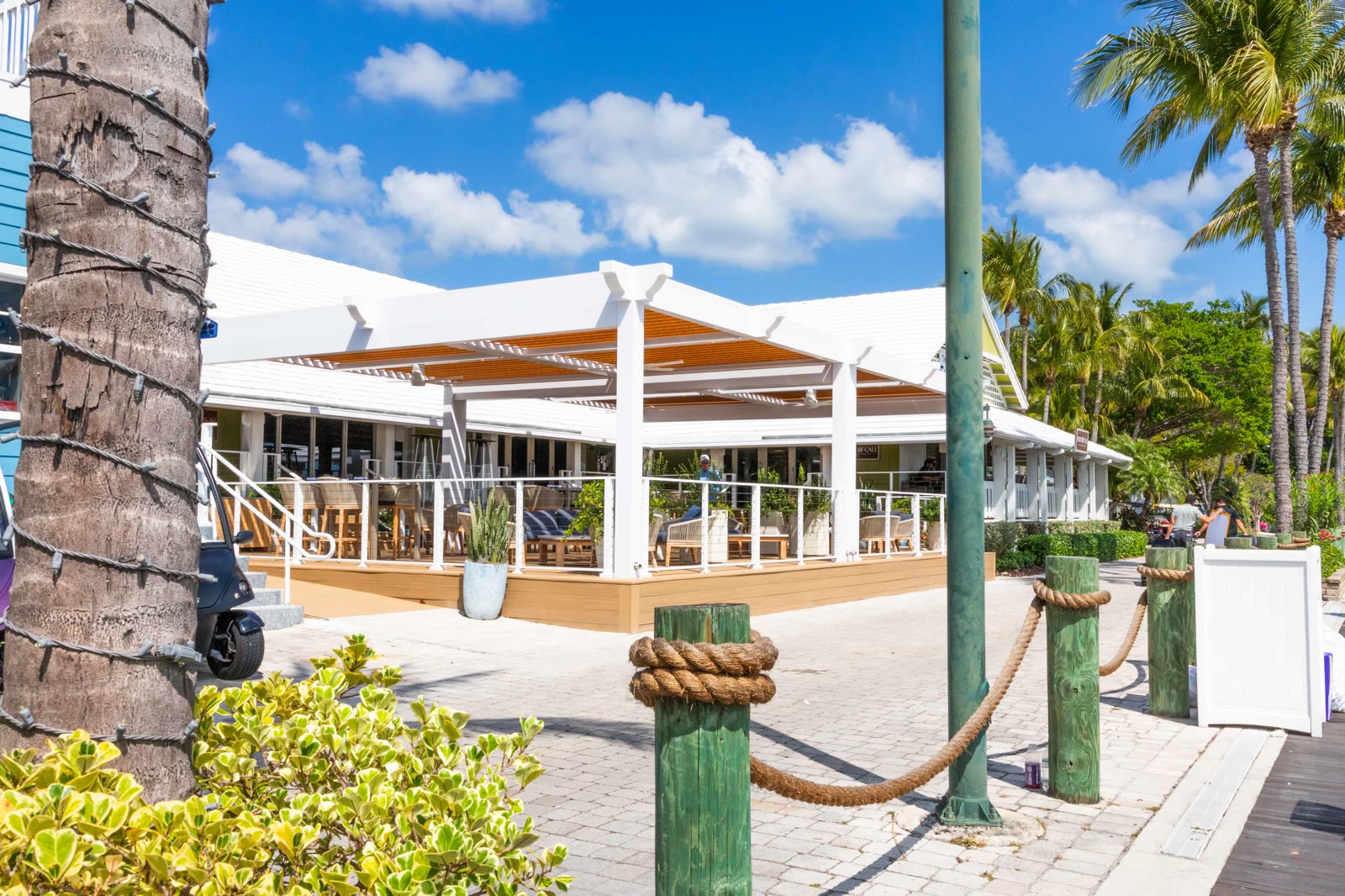 White Azenco R-BLADE pergola over a waterfront restaurant patio. Manufacturer-network installation photo, not a CCSI project.